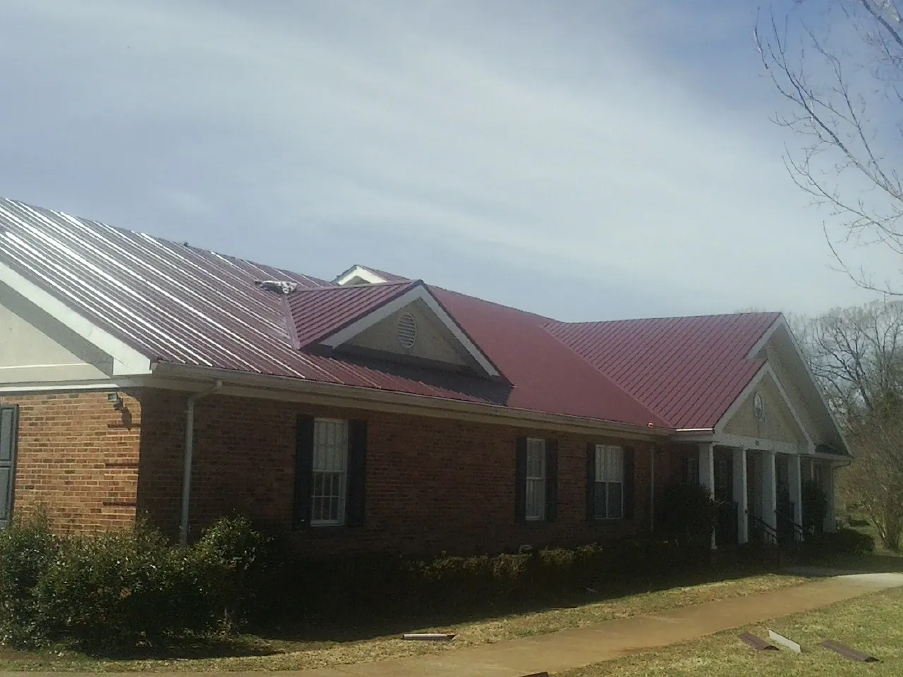 Red metal roof with gabled entries on a long brick building, from a Hail Damage Roof Repair job in Challis