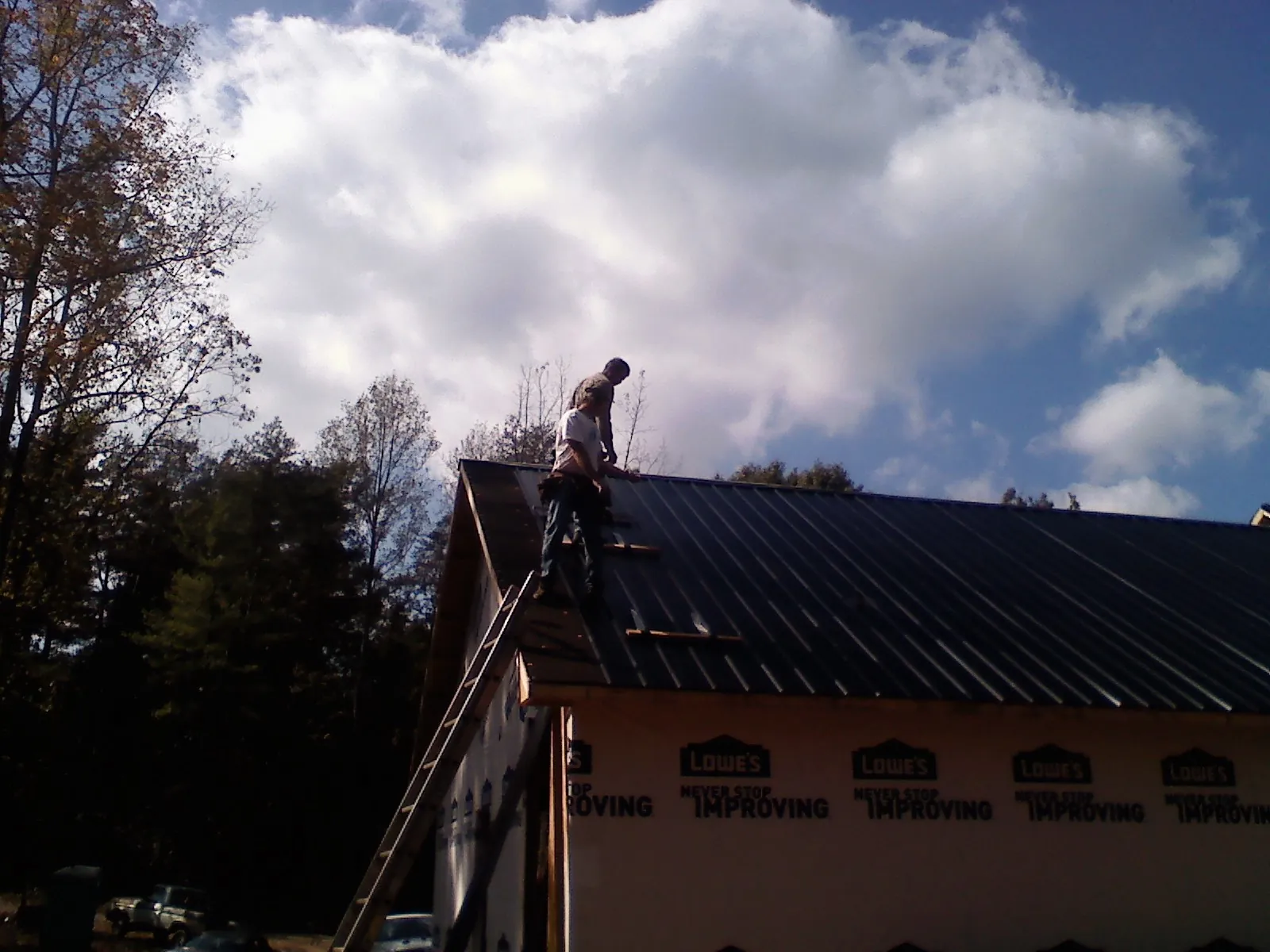 Roofer fastening dark metal panels high against a cloudy sky, from a Roof Inspection job in Challis